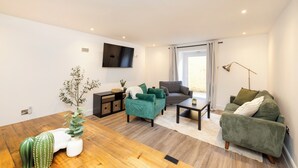 A modern living room with a wooden floor, green sofas, a flat-screen TV, and a large window with curtains. - JOIVY 3BR Flat in Haymarket with Free Parking (Edinburgh)
