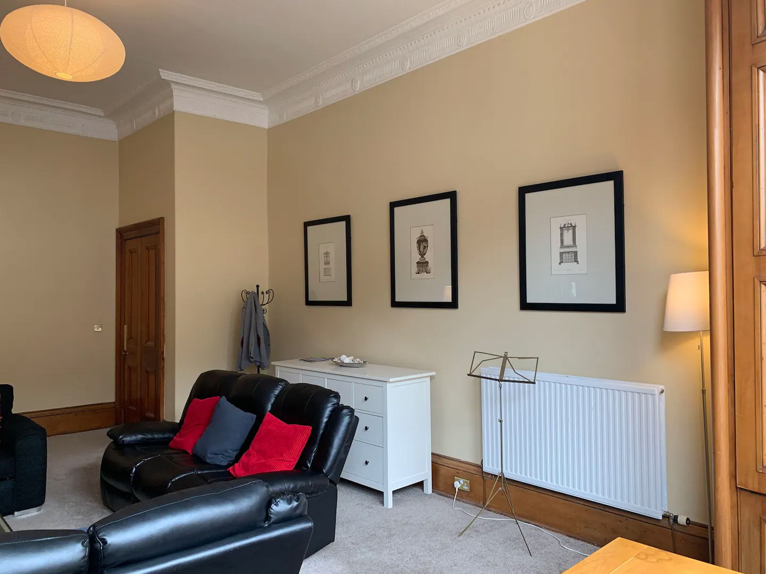 A living room with a black leather sofa, a white dresser, and three framed pictures on the wall.