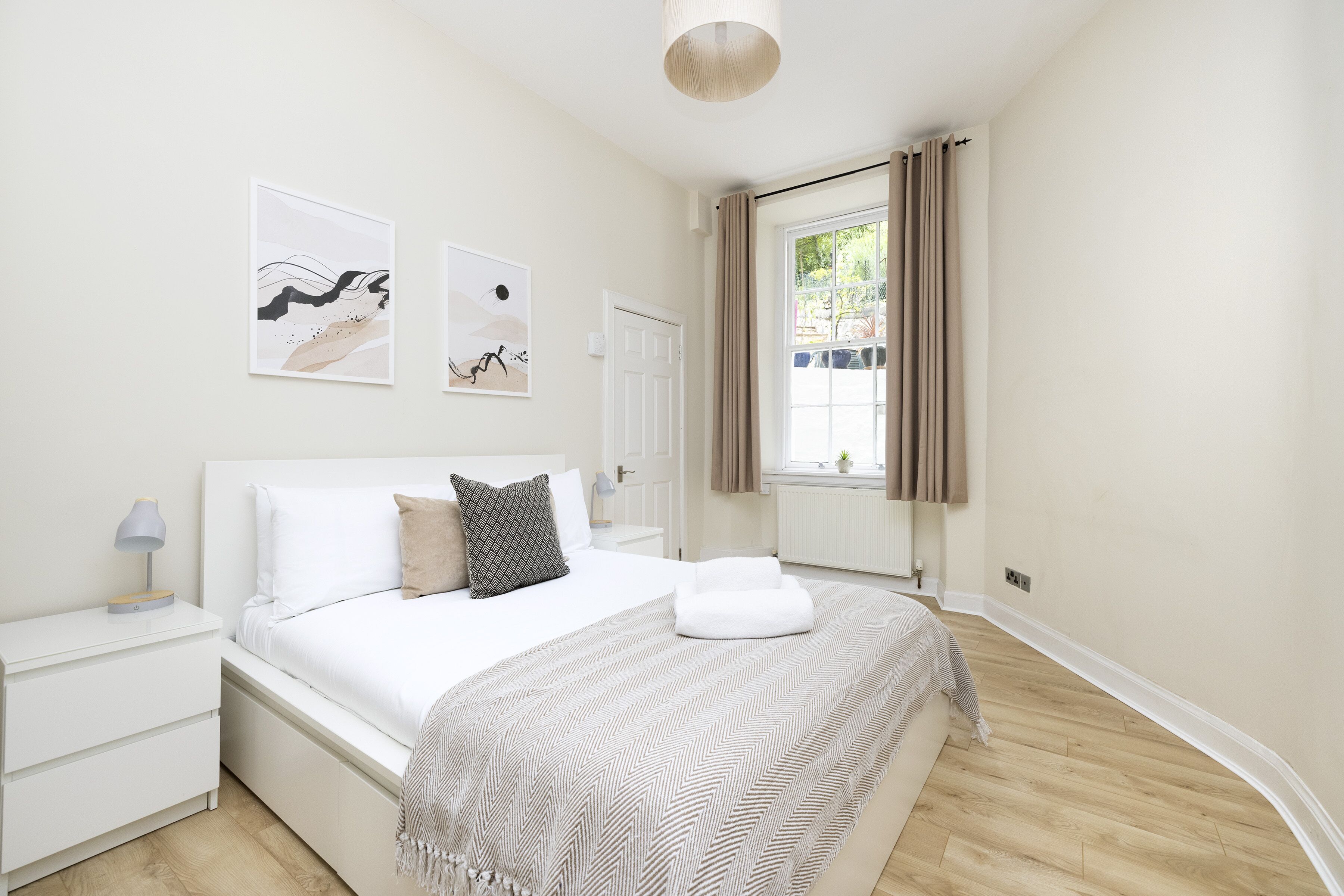 Un dormitorio ordenado con cama, mesitas de noche y cuadros en las paredes.