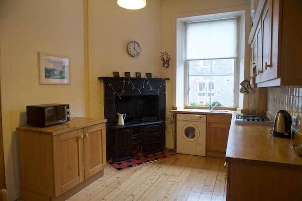 A compact kitchen with wooden cabinets, a microwave, a washing machine, and a window with a view.
