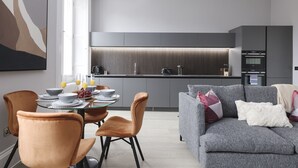 Una cocina moderna con armarios grises, horno empotrado y comedor con mesa y sillas de vidrio.