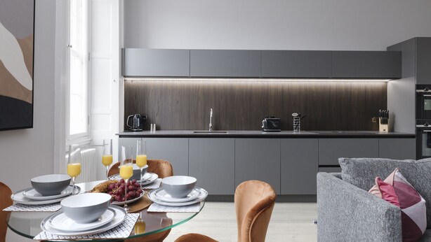 Una cocina moderna con armarios grises, una mesa de comedor de vidrio y un sofá gris.