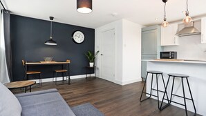 Une cuisine moderne équipée d’un four à micro-ondes, un coin repas avec une table et des chaises, et un salon avec un canapé et un tapis.
