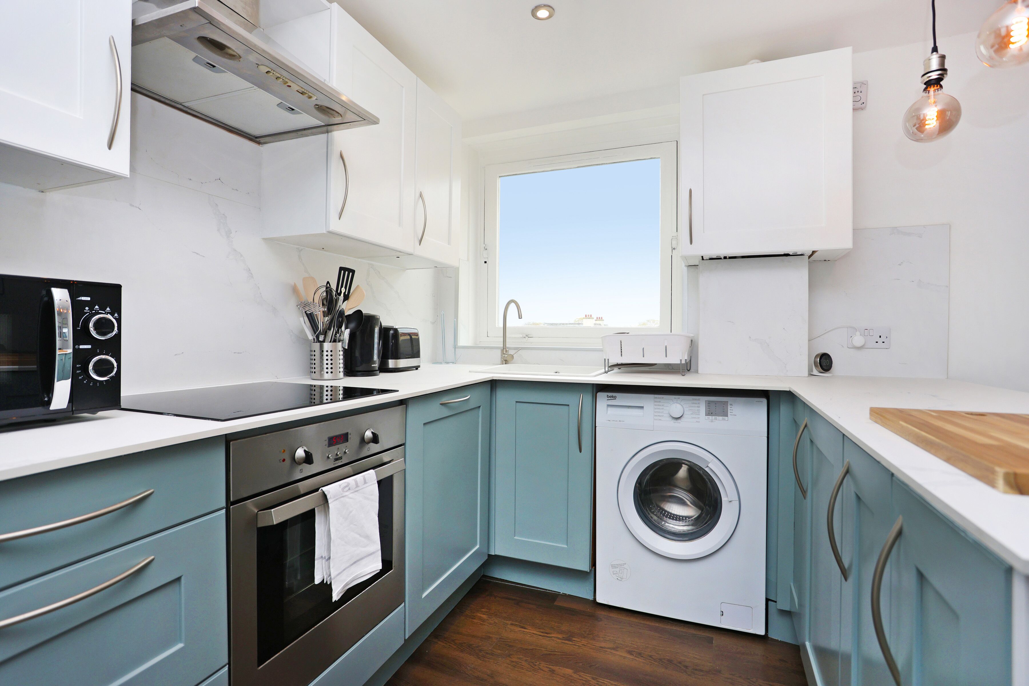 A modern kitchen with a built-in washing machine, stainless steel appliances, and light blue cabinets.