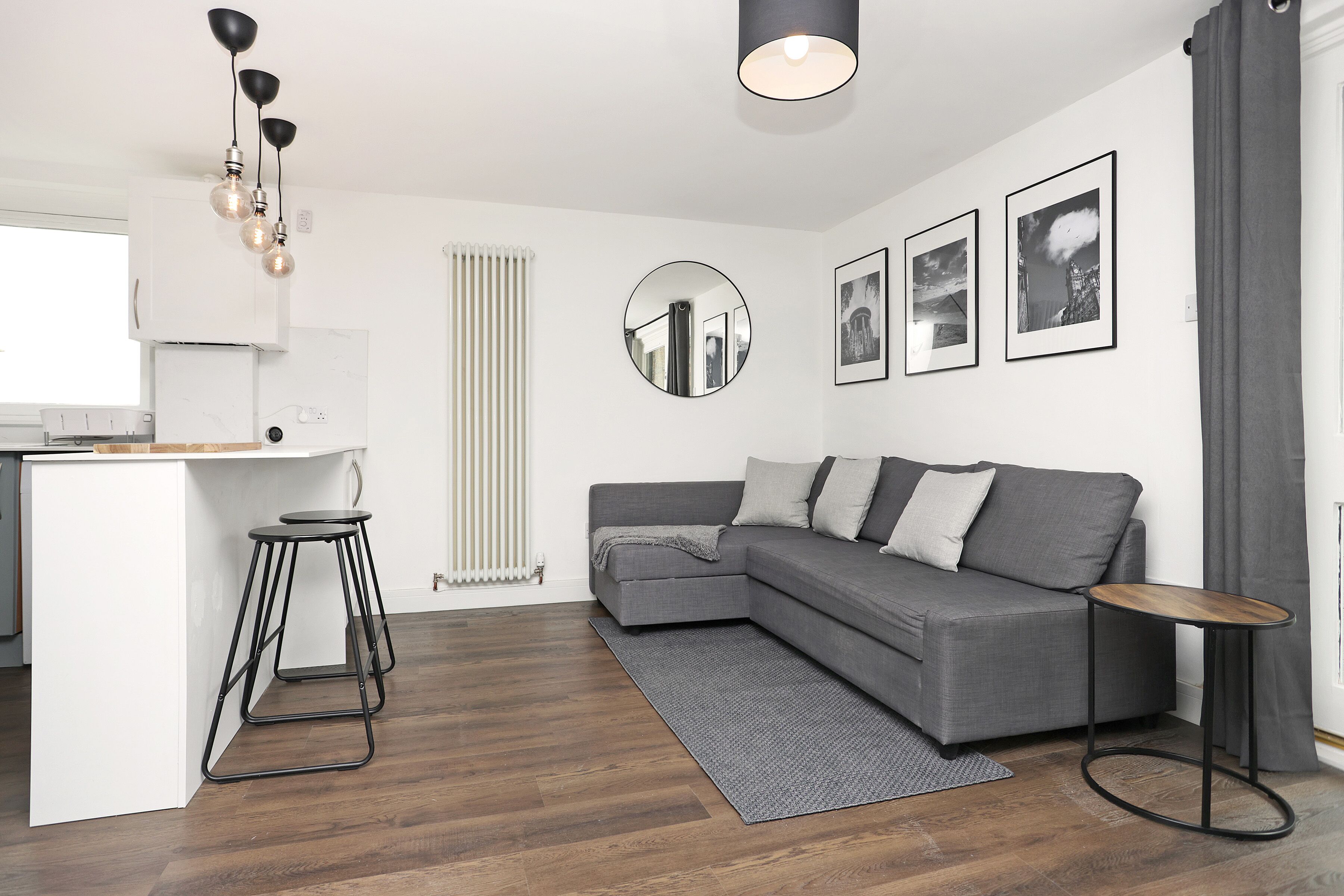 A modern living room with a grey sofa, a round mirror, and a small wooden side table.
