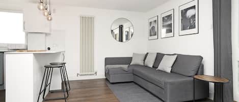 A modern living room with a grey sofa, a round mirror, and a small wooden side table.