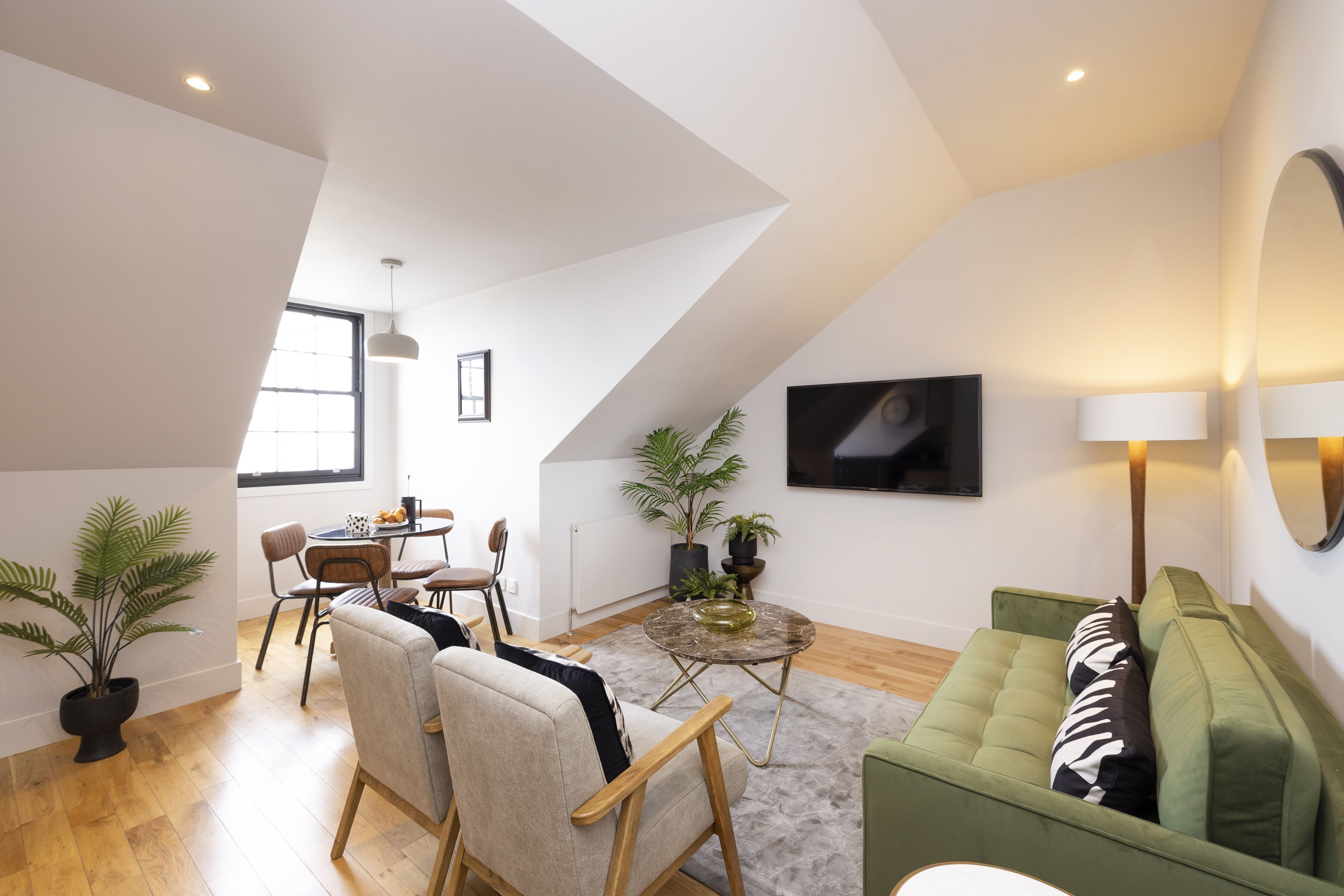 Um apartamento moderno tipo loft com área de jantar, sofá verde e uma janela grande que proporciona iluminação natural.
