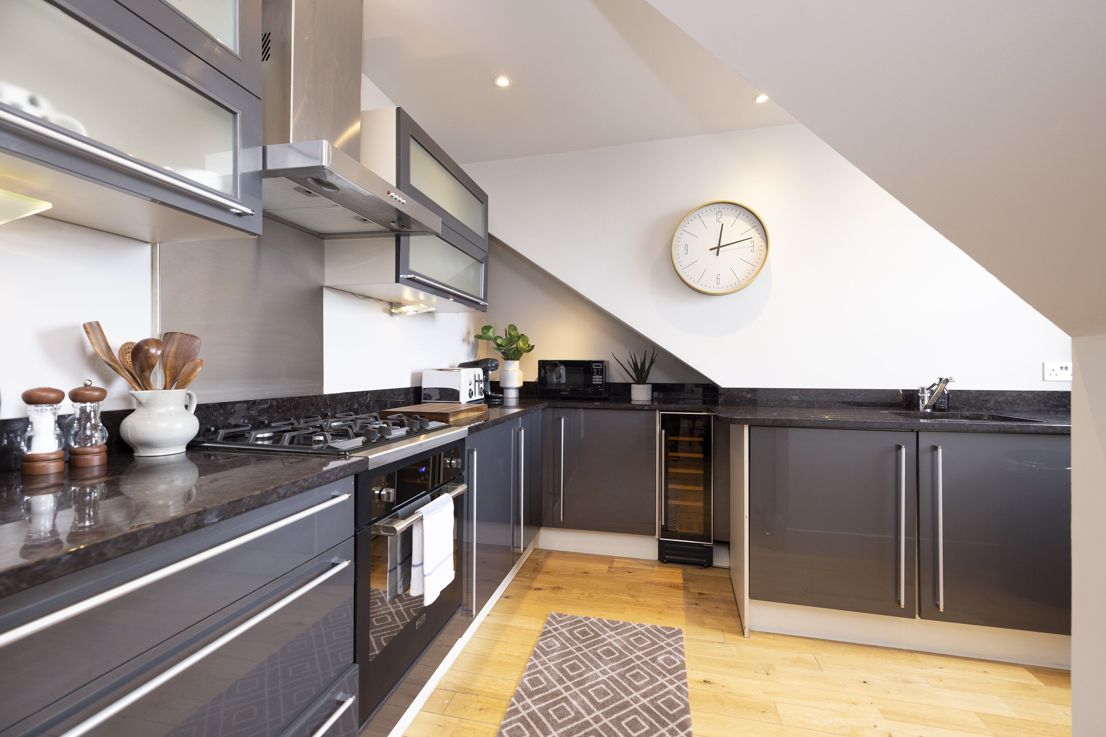 A modern kitchen with dark cabinets, stainless steel appliances, and a wooden herringbone floor.