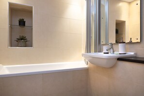 Ein modernes Badezimmer mit einer weißen Badewanne, einem Waschbecken mit Spiegel und einem Regal mit zwei Topfpflanzen.