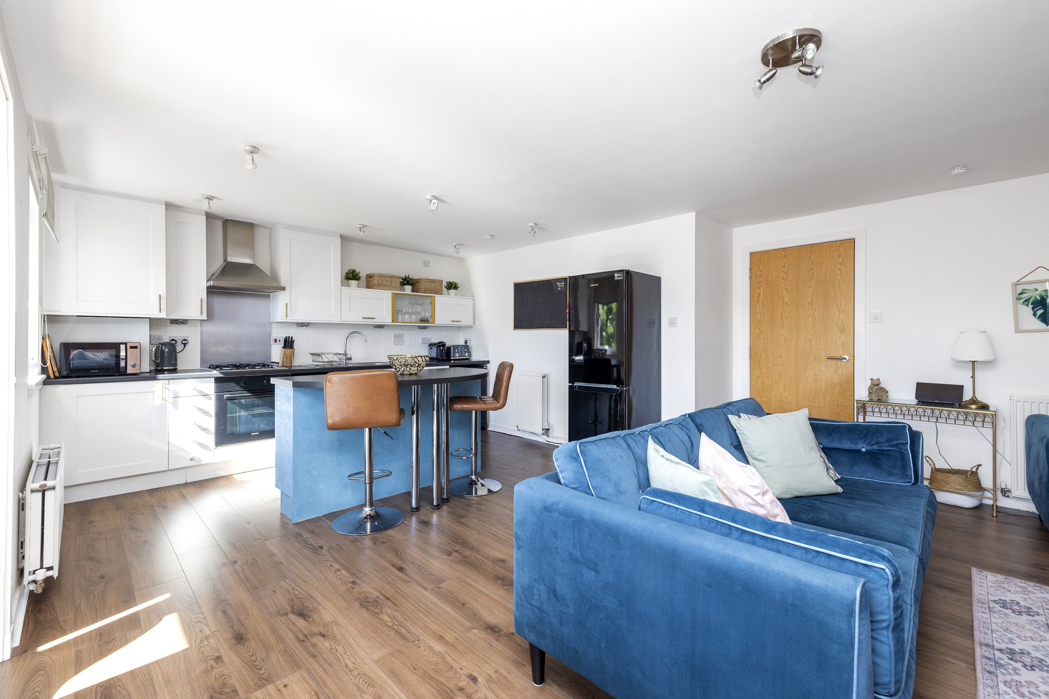 A modern kitchen with white cabinets, a black refrigerator, and a blue sofa in the living area.