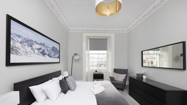 A modern bedroom with a large bed, a desk, a chair, a dresser, a large mirror, and a framed picture on the wall. - JOIVY 4-Bed Stylish Flat In Edinburgh City Centre (Edinburgh)