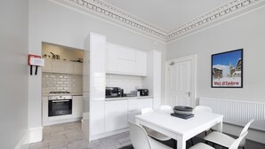 A modern kitchen with white cabinets, a dining table with chairs, and a framed picture on the wall. - JOIVY 4-Bed Stylish Flat In Edinburgh City Centre (Edinburgh)