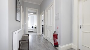 A hallway with a fire extinguisher mounted on the wall, a framed picture, and a radiator. - JOIVY 4-Bed Stylish Flat In Edinburgh City Centre (Edinburgh)