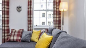A gray sofa with yellow and red plaid cushions, a floor lamp, and plaid curtains. - JOIVY Heart Of Grassmarket 1 Br Apartment (Edinburgh)
