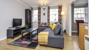 A modern living room with a grey sofa, a flat-screen TV, a coffee table, and a fireplace. - JOIVY Heart Of Grassmarket 1 Br Apartment (Edinburgh)