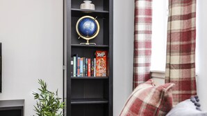 A room with a black bookshelf containing books and a globe, a potted plant, and a plaid curtain. - JOIVY Heart Of Grassmarket 1 Br Apartment (Edinburgh)