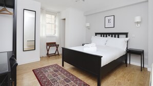 A bedroom with a bed, a nightstand, a chair, a desk, a mirror, and a chandelier. - JOIVY Heart Of Grassmarket 1 Br Apartment (Edinburgh)