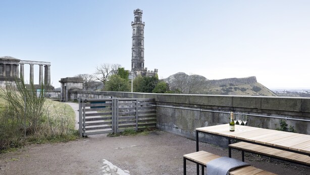 Une terrasse extérieure avec une table et des bancs, offrant une vue sur une tour historique et des ruines.