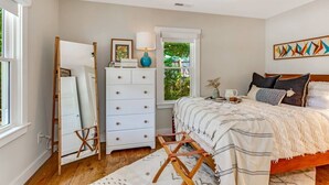 Une chambre à coucher avec un lit, une commode et une fenêtre donnant sur un paysage verdoyant.
