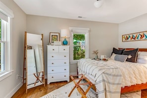 A bedroom with a bed, dresser, and a window with a view of greenery.