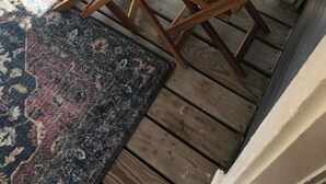 Une terrasse en bois avec une table ronde et des chaises, un tapis et un petit coin jardin.