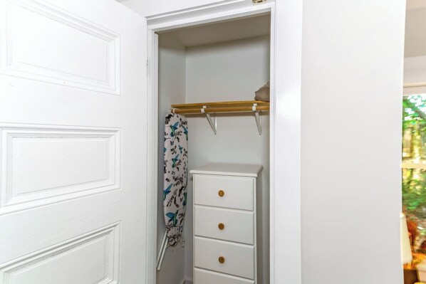 A white closet with a hanging rod, a white dresser with three drawers, and a patterned shower curtain.