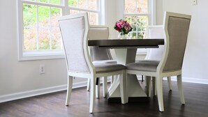 A dining area with a white table and chairs, large windows, and a vase with flowers. - Spacious, Relaxed 5 Bedroom Getaway (LILBURN)