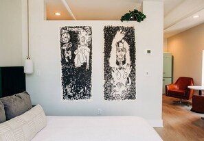 Moderni hotellihuone, jossa on suuri sänky, punainen tuoli ja kaksi abstraktia taideteosta seinällä.