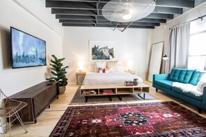 A modern bedroom with a bed, bedside tables, a blue sofa, a large rug, and a painting on the wall.
