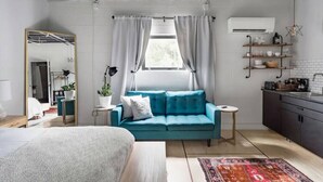A modern bedroom with a bed, a blue sofa, a small table, a mirror, and a window with curtains.