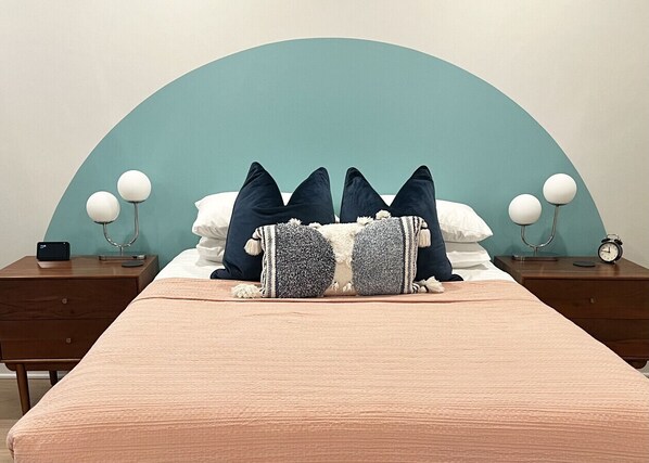 A bed with a teal headboard, two bedside tables with lamps, and a clock on one table.