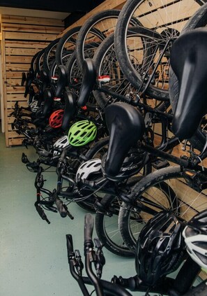 A row of bicycles with helmets, some with visible brand logos, parked in a room with wooden slats on the wall.
