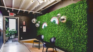 Un espace d’accueil agrémenté d’un mur végétal, de chaises noires et d’un plafond avec des poutres apparentes et des luminaires.