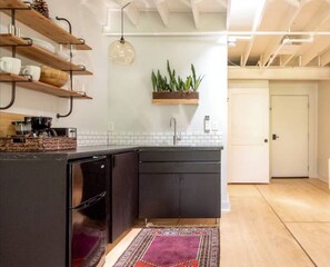 A modern kitchen with dark cabinetry, a built-in sink, and a wooden shelf with dishes.