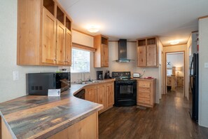 A compact kitchen with wooden cabinets, a built-in oven, and a refrigerator. - Mobile Home E-1 at Safe Harbor Brady Mountain on Lake Ouachita! (Royal)
