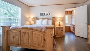 A bedroom with a wooden bed, two bedside tables with lamps, a 'RELAX' sign on the wall, and a view of the outside through a window with blinds.