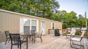 A covered deck with a table and chairs, a barbecue grill, and a small building with windows and a door.