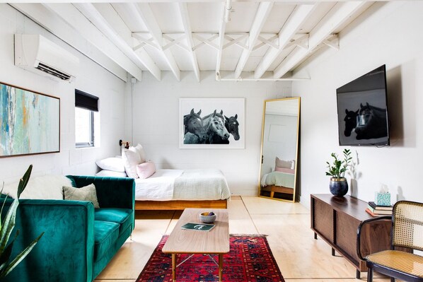 Un dormitorio moderno con cama, sofá verde, una mesita de centro y obras de arte en las paredes.