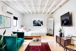 Un dormitorio moderno con cama, sofá verde, una mesita de centro y obras de arte en las paredes.