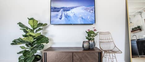 A living room with a large TV on the wall, a wooden cabinet, a large potted plant, a chair, and a mirror.