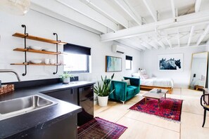 Un apartamento moderno con cocina, sala de estar y dormitorio. Hay estantes de madera sobre la encimera de la cocina, un ventanal grande y un cuadro de caballos en la pared.