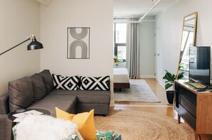 A modern living room with a sofa, a black floor lamp, and a geometric wall art piece. - Market #1 · Stellar Suites | King Loft | NuLu | Boutique Hotel (Louisville)