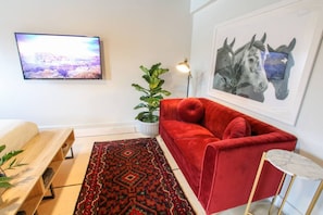 A modern living room with a red sofa, a patterned rug, a potted plant, a mounted TV, and a framed artwork. - Market #6 · Stellar Suites | Ruby King Suite in NuLu | Bikes (Louisville)