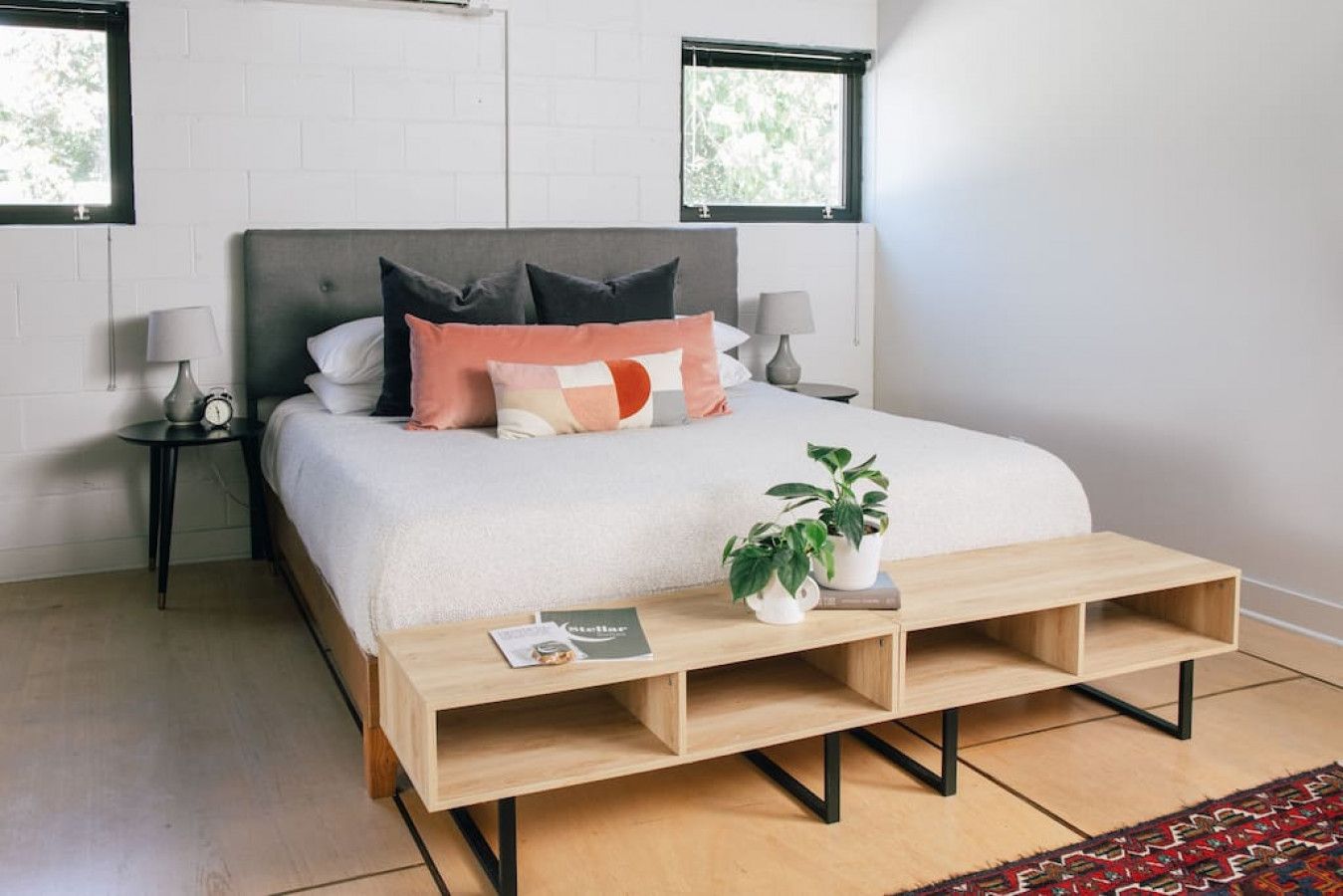 A bedroom with a bed, bedside tables, a nightstand, a wooden coffee table, and a potted plant.