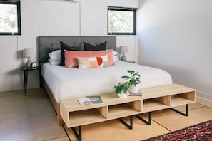 Ein Schlafzimmer mit einem Bett, Nachttischen, einem kleinen Tischchen, einem Holztisch und einer Topfpflanze.