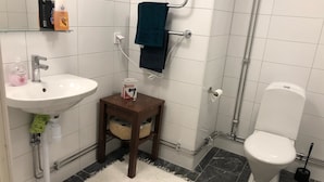 Ein Badezimmer mit einem weißen Waschbecken, einem kleinen hölzernen Hocker mit Toilettenpapier, einem Handtuchhalter und einer Toilette.