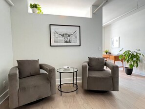 Ein modernes Wohnzimmer mit zwei grauen Sesseln, einem kleinen runden Tisch und einem gerahmten Bild an der Wand.