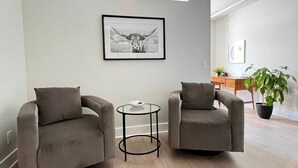 Una sala de estar moderna con dos sillones grises, una mesita redonda y un cuadro enmarcado en la pared.