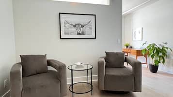 Ein modernes Wohnzimmer mit zwei grauen Sesseln, einem kleinen runden Tisch und einem gerahmten Bild an der Wand.