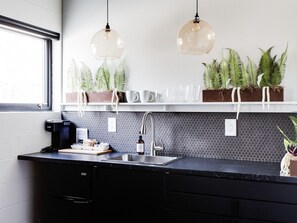 Eine moderne Küche mit schwarzem Arbeitsplatz, Spüle aus Edelstahl und zwei Pendelleuchten.